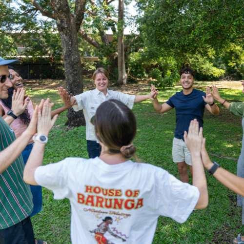 Group of people outdoors playing a hands-up group activity on grass.